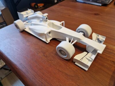 Weißes 3D-gedrucktes Modell eines Formel 1 Rennwagens aus Resin. Detailreiche Nachbildung mit Reifen, Front- und Heckflügel, platziert auf einem Holztisch.