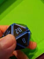 „Nahaufnahme eines blauen Squishy D20 Fidget Würfels mit schimmerndem Glitzereffekt, gehalten in einer Hand auf grünem Hintergrund