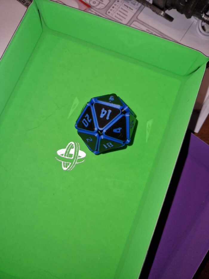 Blauer Squishy D20 Fidget Würfel mit Glitzereffekt auf Würfelmatte Blauer Squishy D20 Fidget Würfel mit funkelnden Reflexen, liegend auf einer grünen Würfelmatte – besonderes Zubehör für Tabletop und D&D.
