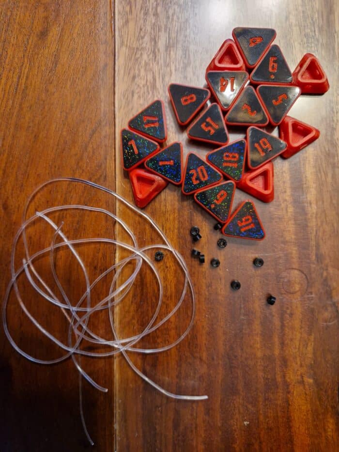 DIY Fidget D20 Würfel Bausatz – Zerdrückbarer Tabletop Würfel zum Selbstbauen | RPG & DnD Zubehör DIY Bausatz für einen Fidget D20 Würfel – zerdrückbarer Stresswürfel für Tabletop, bestehend aus roten und schwarzen Würfelsegmenten, Verbindungsschläuchen und Kleinteilen auf Holztisch.